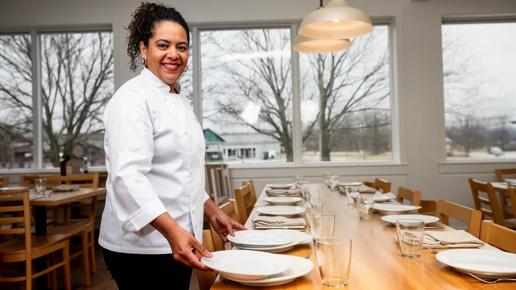 A woman with dark curly hair tied back who owns a small family restaurant at work.